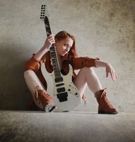 Learn To Play A Guitar Fast - A woman sitting on the floor, holding an electric guitar.