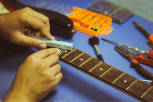 A photo of someone polishing the frets on an electric guitar neck