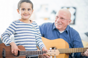 Learning Guitar For Seniors - A child and his grandfather playing music together.