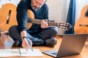 Learning Guitar For Seniors - A man learning to play the guitar using sheet music and a laptop.