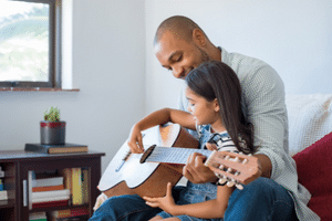 Guitar Tips For Beginners - A child being taught to play the acoustic guitar by an adult.