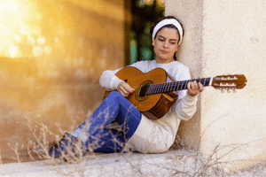 Relax When Playing Guitar – A young woman sitting on the ground playing an acoustic guitar