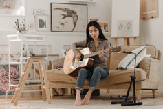 Relax When Playing Guitar – A woman playing  an acoustic guitar on a couch