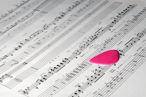 Best Guitar TAB Sites – Sheet music with tablature. A red guitar pick is on top of the music.