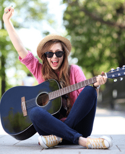 Best Guitar TAB Sites – A woman is sitting on the ground playing an acoustic guitar and looking very excited.