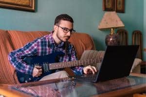 Best Guitar TAB Sites – A man sitting on a couch with an electric guitar and a laptop computer.