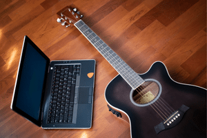 A laptop computer on the floor next to an acoustic guitar.