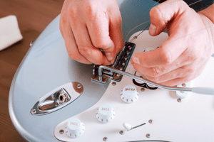 How To Set Up An Electric Guitar - A player is making adjustments to the bridge saddles of an electric guitar.