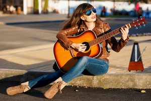 Reduce Guitar String Noise – A woman playing an acoustic guitar with a metronome.