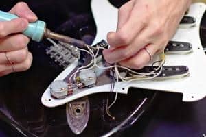 Super Strat Guitars - A photo showing someone making electronic modifications to an electric guitar
