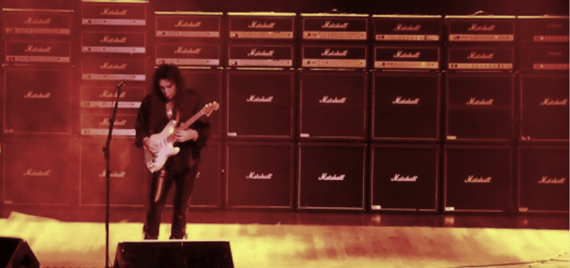 Can You Play An Electric Guitar Unplugged - Yngwie Malmsteen standing in front of a wall of Marshall amps